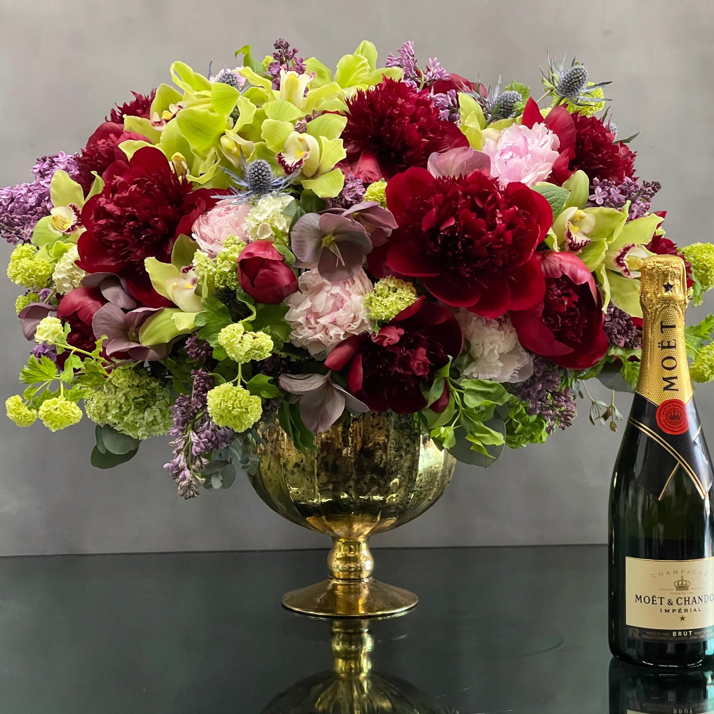 Our Lovely Together arrangement is available for same day delivery! This is a double sided arrangement on a gold pedestal bowl. Floral includes burgundy and pink peonies, cymbidium orchids, thistle, and Lilac. Flowers may vary depending on the season. An absolute gesture of love and romace, perfect for anniversary, birthday and I'm sorry. 