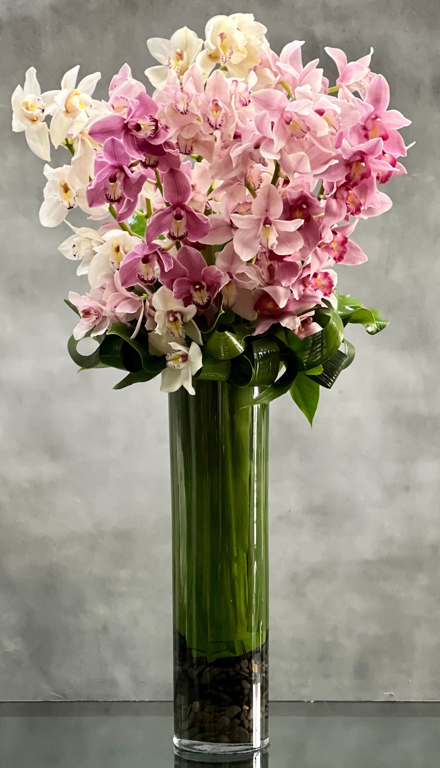 Deliver happiness and joy with this magnificent floral design from Santa Monica Florist ! This arrangement is offered for same day delivery. This arrangement features a modern tall leaf lined vase overflowing with 10 tall stems of gorgeous pink, lavender and white Cymbidium Orchids. Unique and breathtakingly beautiful! Perfect for Birthdays, Love and Romance, and Thank you !