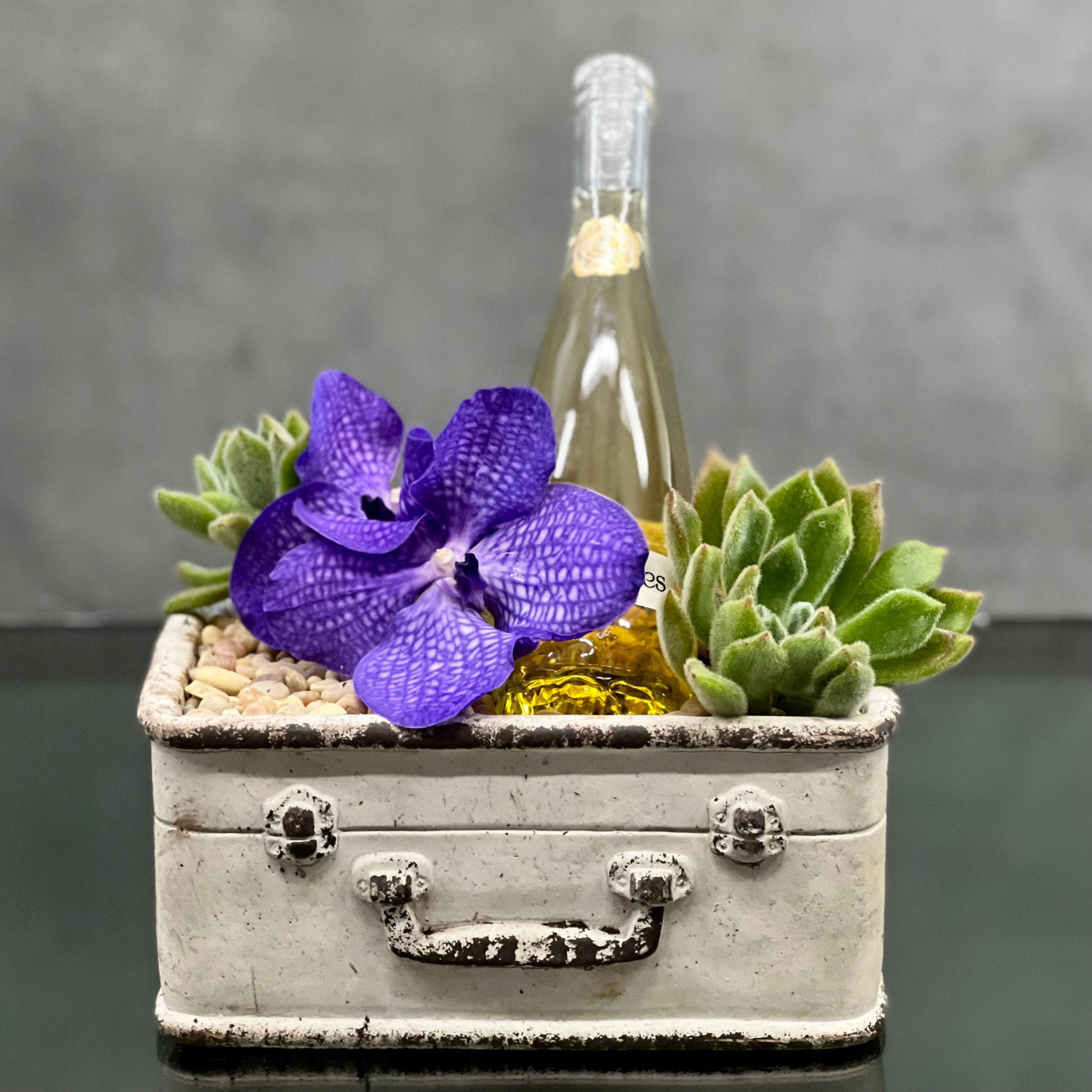 Santa Monica Florist presents One for the Road for same day delivery. This is the perfect arrangement for congratulation flowers, get well flowers, Welcome home flowers. Includes, Vanda Orchid, Bottle of Champagne  placed in a suitcase planter !