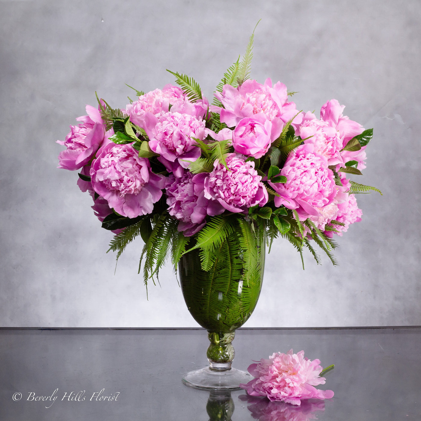 Elegant pink peony arrangement in a clear 12-inch glass vase with umbrella ferns and Gardenia foliage.