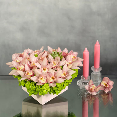 A Pink Delicate Touch arrangement with pink cymbidium orchids, hydrangeas, and succulent in a heart-shaped box, modern same-day delivery by Santa Monica Florist.