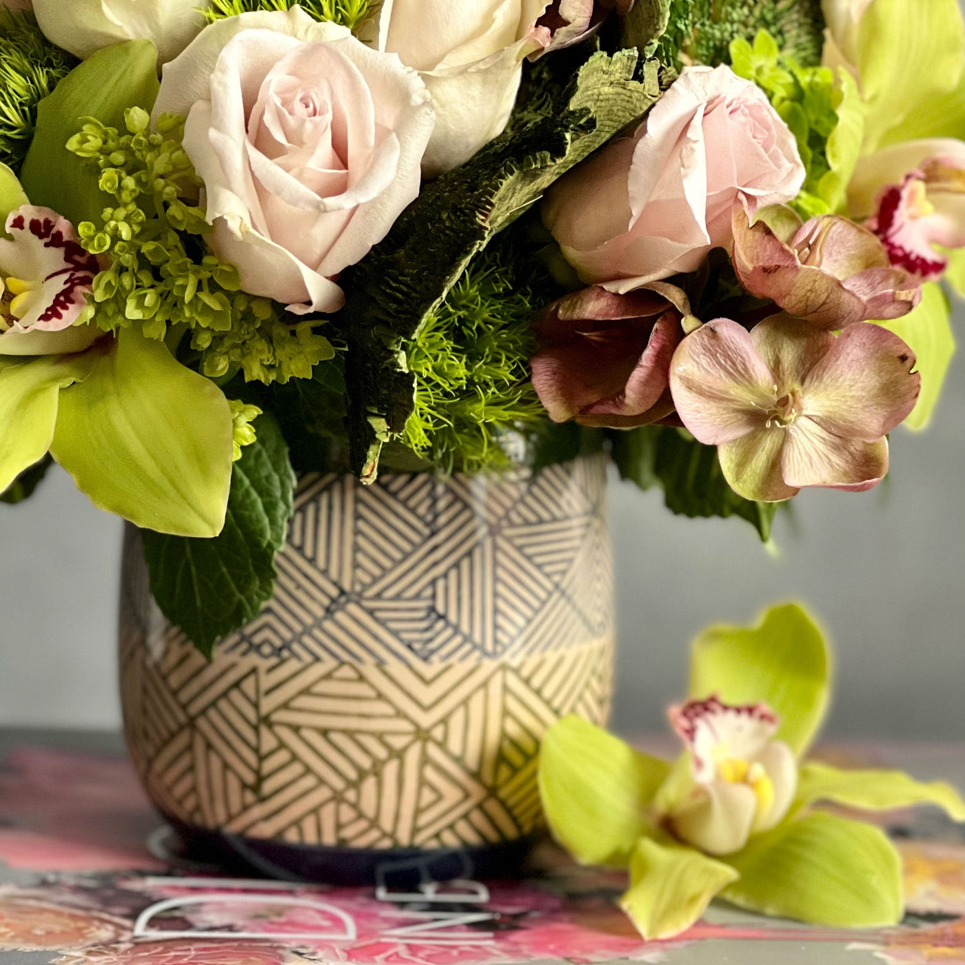 A Rustic Romance arrangement with cream roses, green cymbidium orchids, and seasonal greens in a geometric earth-toned vase, same-day delivery by Santa Monica Florist.