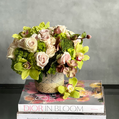 A Rustic Romance arrangement with cream roses, green cymbidium orchids, and seasonal greens in a geometric earth-toned vase, same-day delivery by Santa Monica Florist.