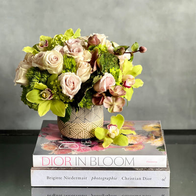 A Rustic Romance arrangement with cream roses, green cymbidium orchids, and seasonal greens in a geometric earth-toned vase, same-day delivery by Santa Monica Florist.