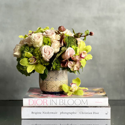 A Rustic Romance arrangement with cream roses, green cymbidium orchids, and seasonal greens in a geometric earth-toned vase, same-day delivery by Santa Monica Florist.