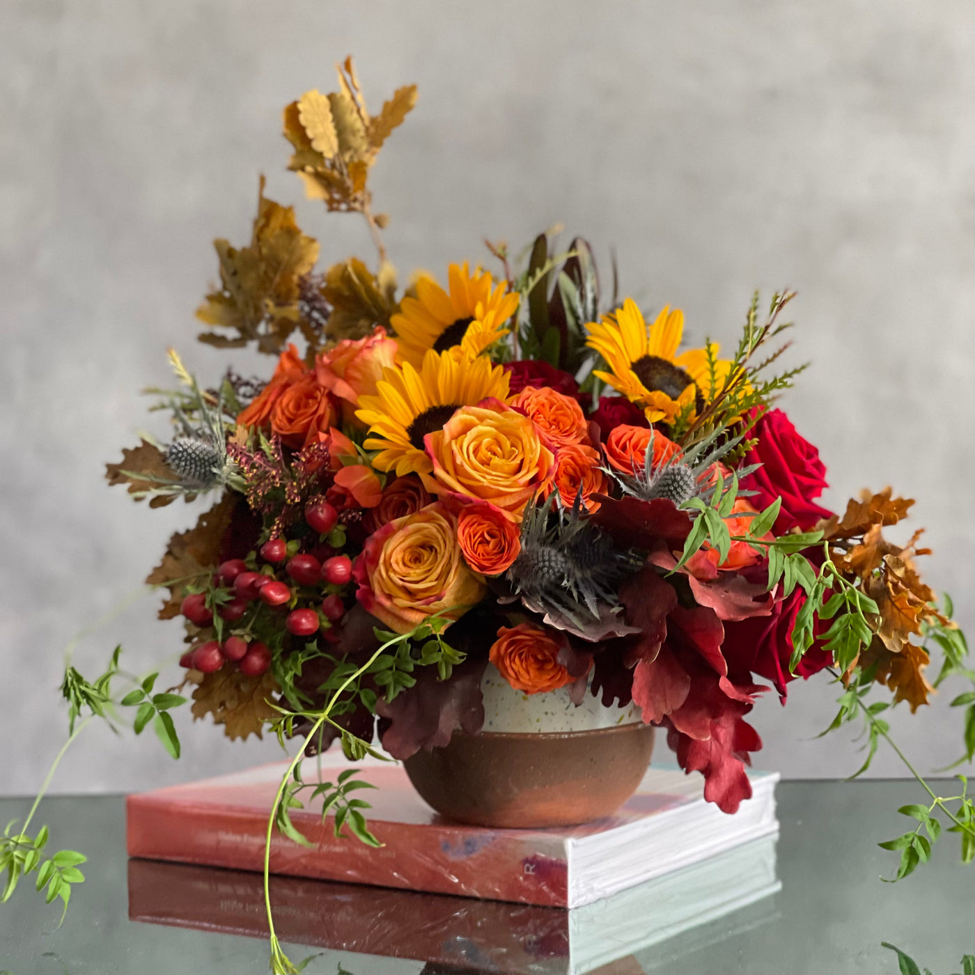 Autumn in the Air arrangement with orange, yellow, and red roses, sunflowers, and fall foliage in a ceramic vase, available for same-day delivery in 90403. Santa Monica Florist  410 Wilshire Blvd  Santa Monica  90403