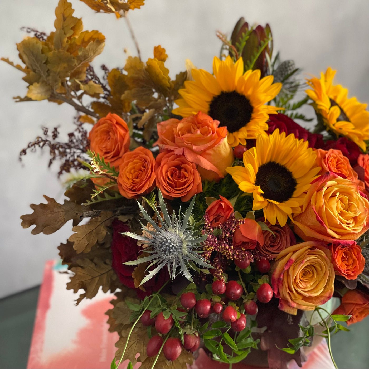 Autumn in the Air arrangement with orange, yellow, and red roses, sunflowers, and fall foliage in a ceramic vase, available for same-day delivery in 90210.