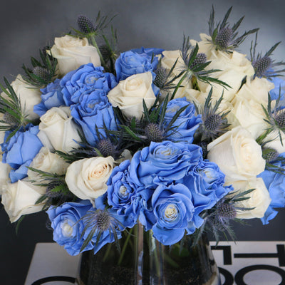 Blue Me Away arrangement with blue and white roses, thistles, and colored sand in a modern vase, available for same-day delivery by Santa Monica Florist.