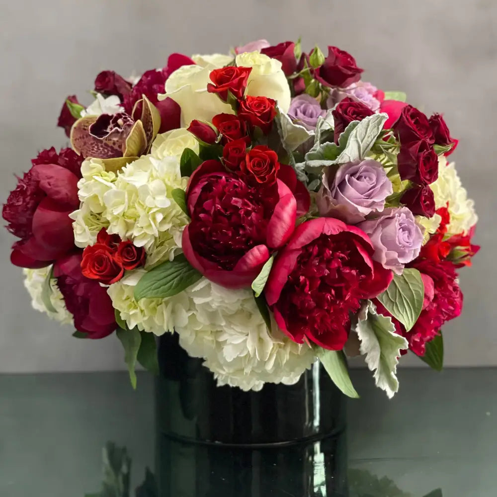 LA Orchidia presents an arrangement that is sure to wow and its available for same day delivery! Our floral piece includes peonies, lavender and white and red roses, cymbidium orchids , nested on hydrangeas in a black cylinder vase. A stunning decoration for any home or office! Or a romantic gesture of love ! 