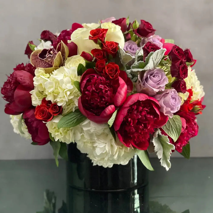 LA Orchidia presents an arrangement that is sure to wow and its available for same day delivery! Our floral piece includes peonies, lavender and white and red roses, cymbidium orchids , nested on hydrangeas in a black cylinder vase. A stunning decoration for any home or office! Or a romantic gesture of love ! 