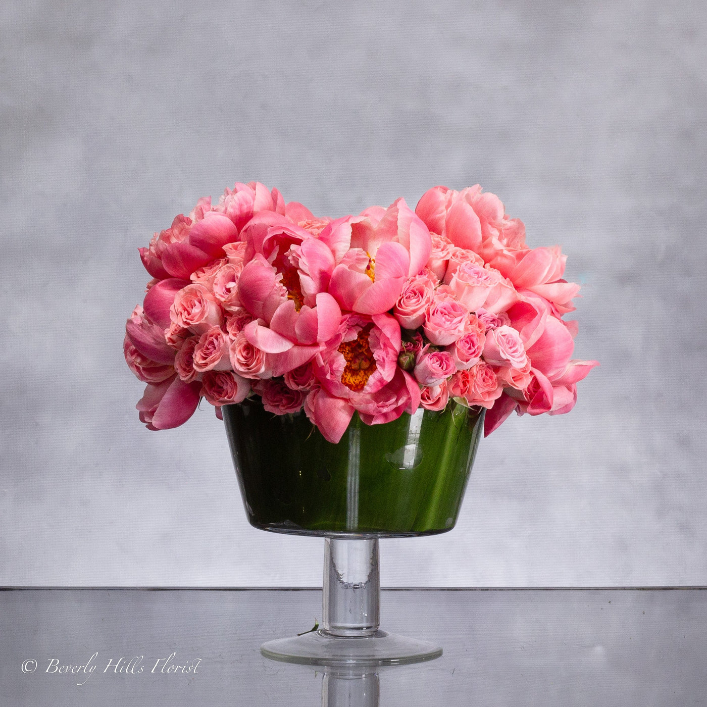 Luxurious arrangement of coral peonies and pink spray roses in a pedestal vase, available for same-day delivery.