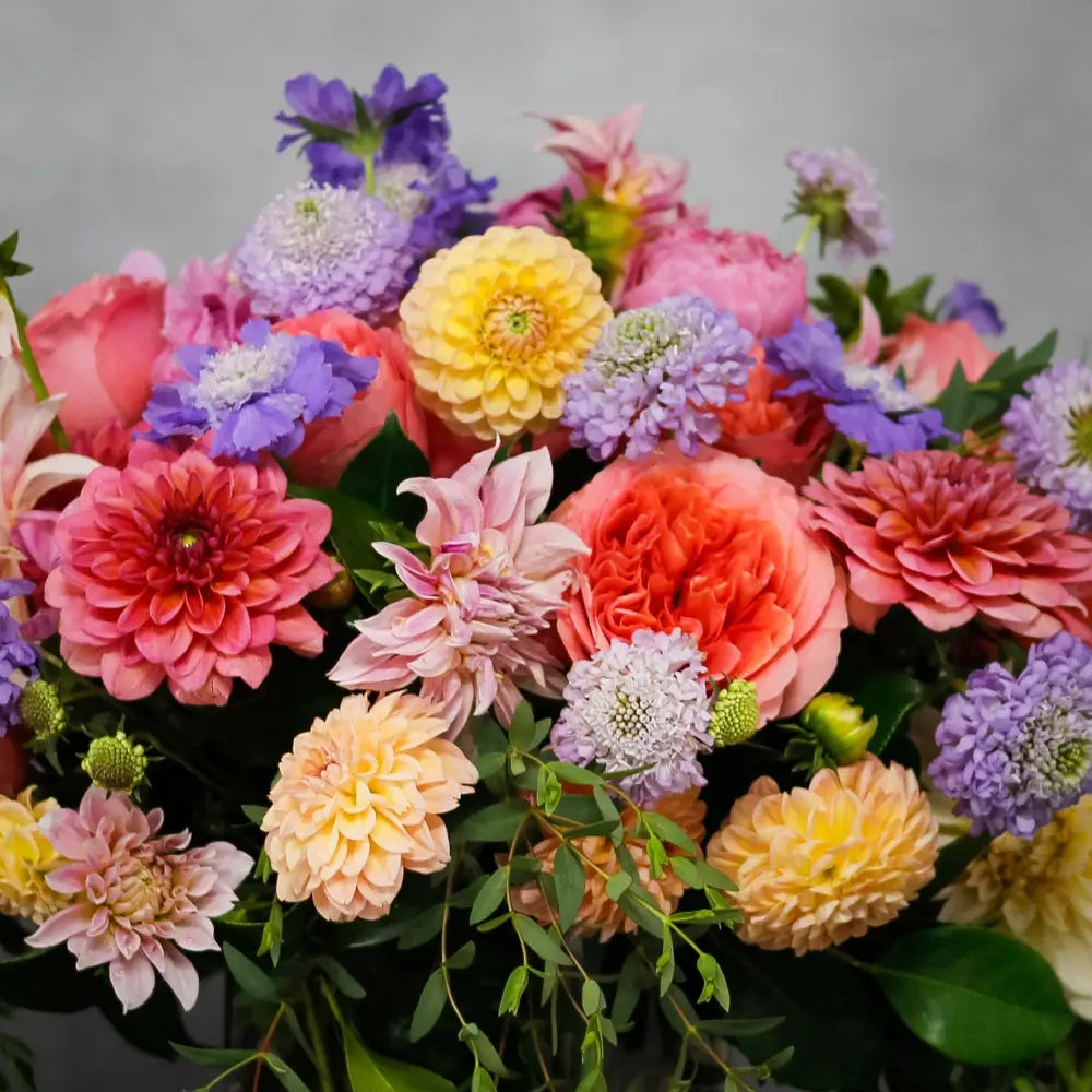 Colorful garden-style flower arrangement with dahlias, peonies, and roses in a glass vase.