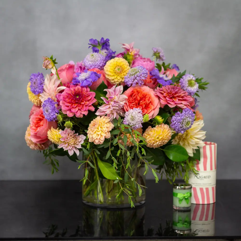 Colorful garden-style flower arrangement with dahlias, peonies, and roses in a glass vase.