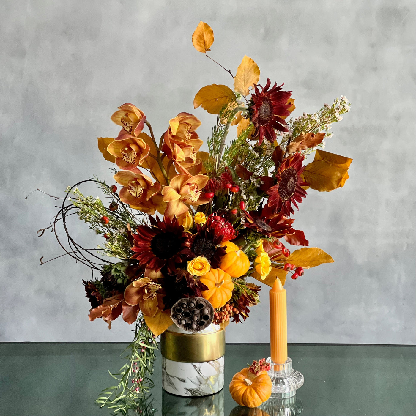 Elegant fall floral arrangement with Dutch Orchids, Black Sunflowers, berries, branches, fall foliage, mini pumpkins, and locally grown flowers in a marble gold container.