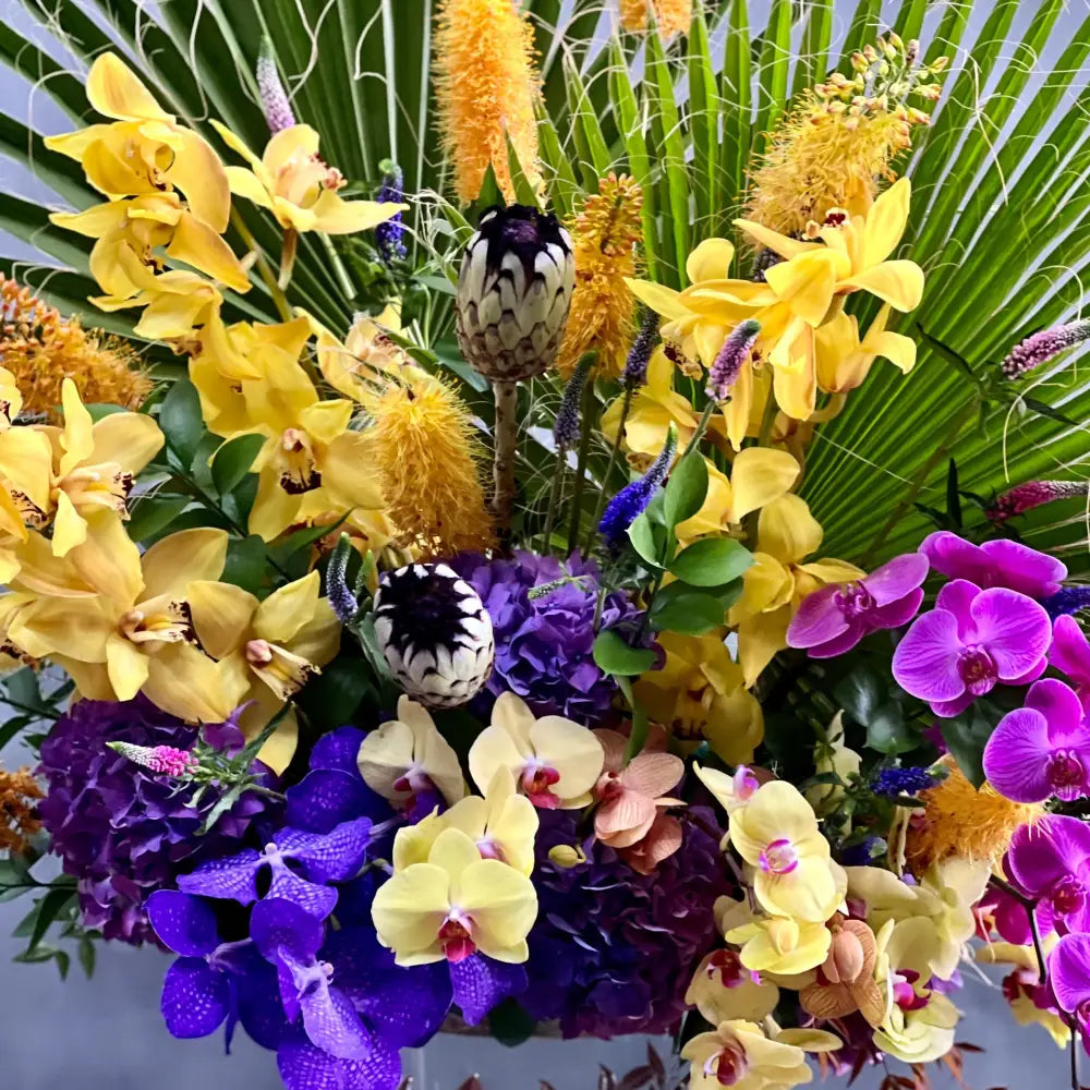 A Spectacular Floral Fantasy featuring extravagant and exotic blooms in tropical colors on a grand scale by LA Orchidia for occasions like congrats, new baby, just because, love and romance. Vibrant seasonal blooms paint the oranges, deep pinks, purples, lime greens and yellow orchids and other floral. Large tropical leaves lined vase with this amazing design and colors. It's a one-of-a-kind, dynamic presentation that will be the center of attention wherever it is placed. Approx: 16 W x 30" H.