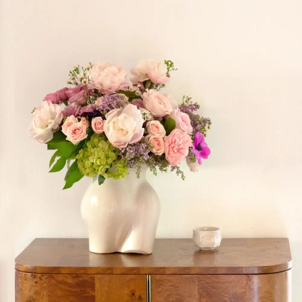 Pink and lavender blooms are a sweet and innocent way to show your affection. LA Orchidia presents same day delivery four our Mademoiselle! Blooms may vary depending on the season. This arrangement features pink and lavender roses, lilacs, and pink peonies with a touch of green hydrangea in a vase that serves as an homage to the curves of the female form. Birthday flowers, Thank you flowers, thinking of you, decor flowers, Love and Romance flowers