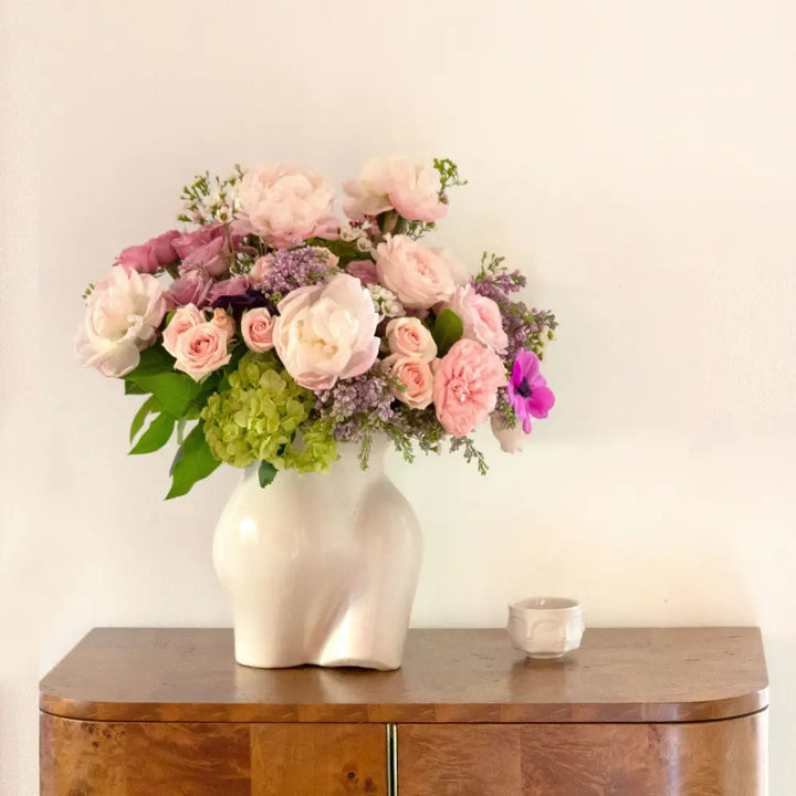 Pink and lavender blooms are a sweet and innocent way to show your affection. LA Orchidia presents same day delivery four our Mademoiselle! Blooms may vary depending on the season. This arrangement features pink and lavender roses, lilacs, and pink peonies with a touch of green hydrangea in a vase that serves as an homage to the curves of the female form. Birthday flowers, Thank you flowers, thinking of you, decor flowers, Love and Romance flowers
