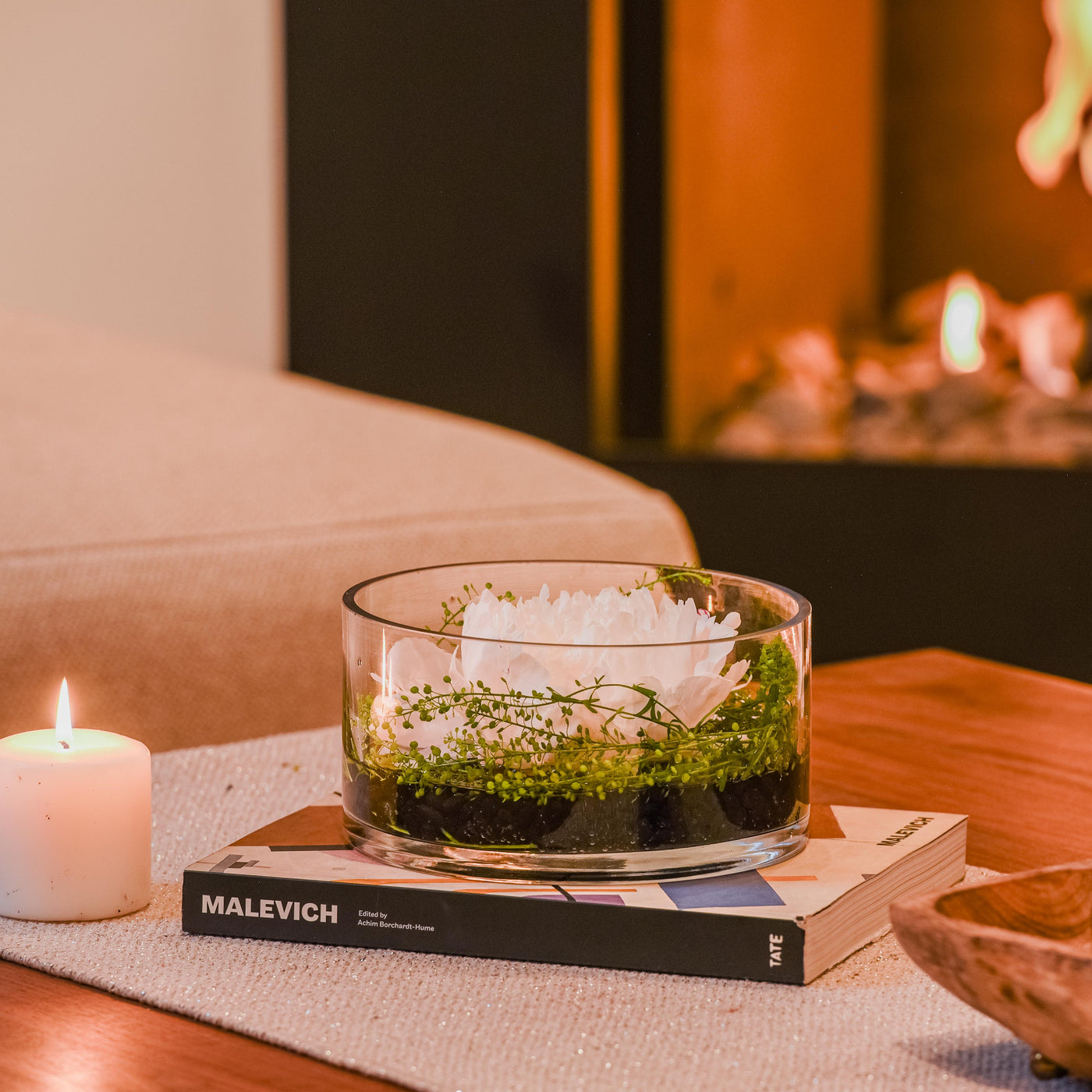 Minimalist white peony arrangement in a circular glass vase with greenery and polished rocks, ideal for tranquility.