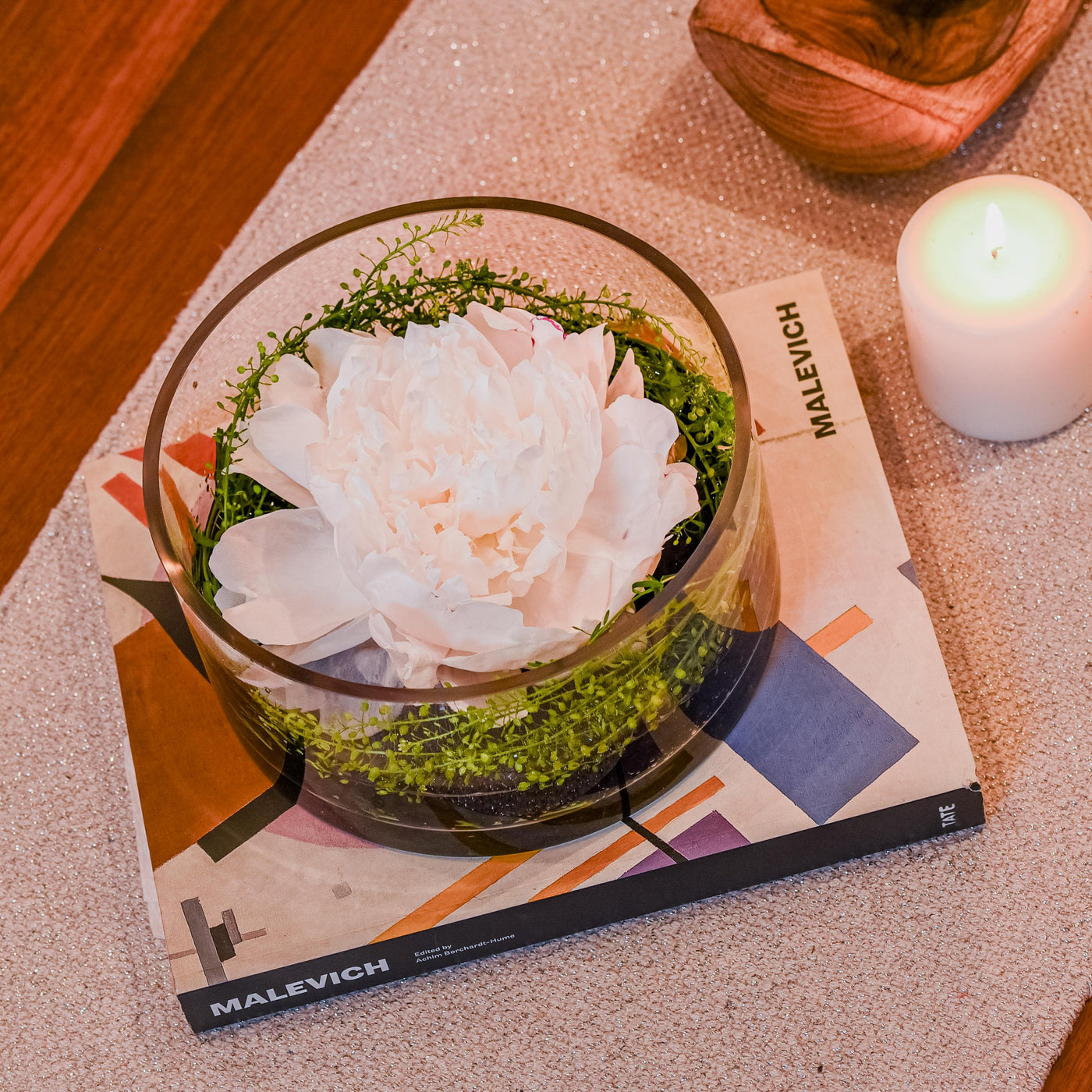 Minimalist white peony arrangement in a circular glass vase with greenery and polished rocks, ideal for tranquility.