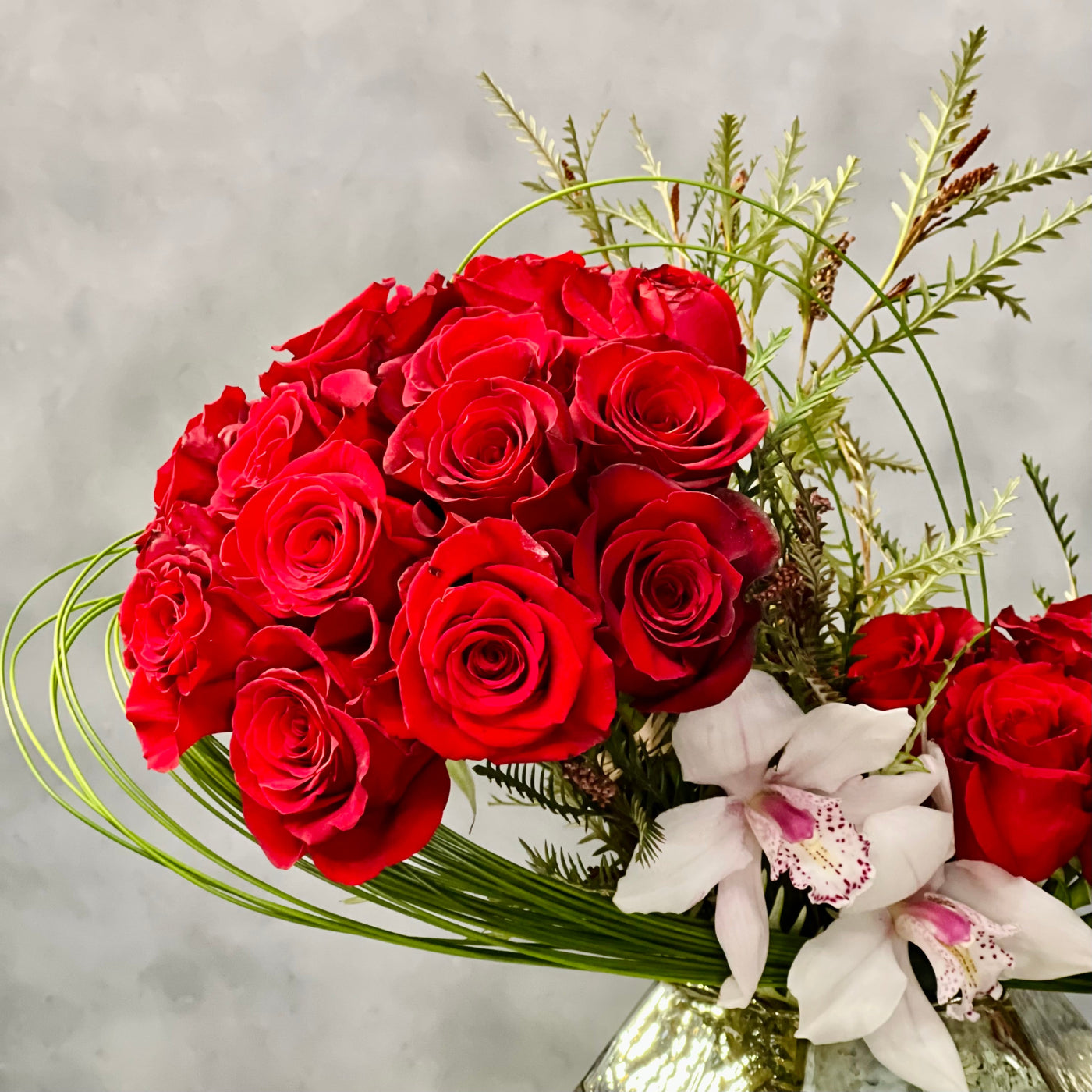 Elegant arrangement of 50 red roses with white Cymbidium orchids and seasonal greens in a geometric vase – Rosalicious by Santa Monica Florist.