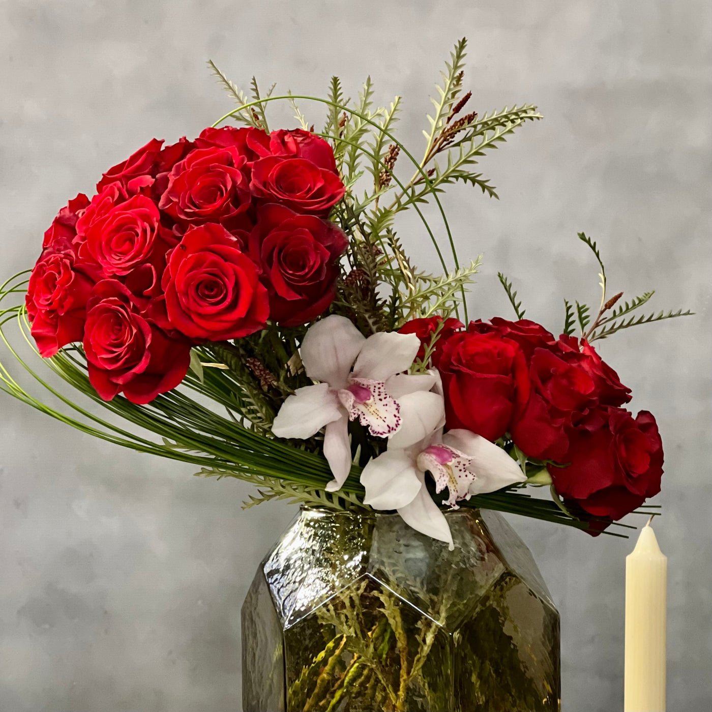 Elegant arrangement of 50 red roses with white Cymbidium orchids and seasonal greens in a geometric vase – Rosalicious by Santa Monica Florist.