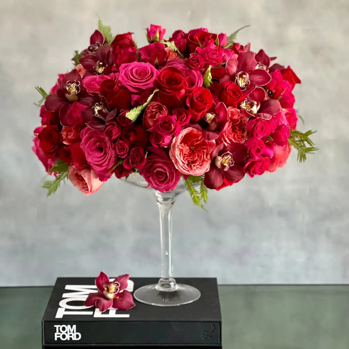Elegant floral arrangement with red and pink roses in a tall pedestal glass vase