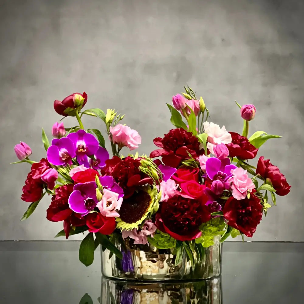 Luxurious Burgundy peony, lavender tulip, and purple orchid arrangement in a silver container.